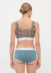 Kvinde med blond hår i en knold iført sports-bh med leopard mønster og blå undertøj med hvid elastik fra Copenhagen Studios, set fra ryggen.