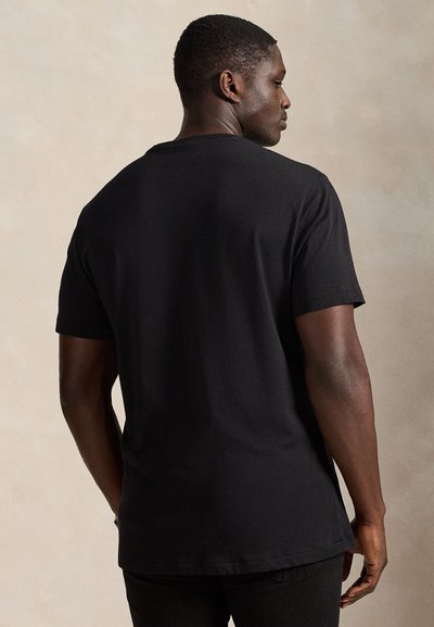 Svart bomulls-T-skjorte med rund hals og korte ermer, med rett kant og minimale sømmer, sett bakfra.