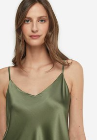 Olivgrön satinlinne med tunna justerbara axelband och V-ringning. Tyget har en slät, glänsande textur med minimal detaljering.