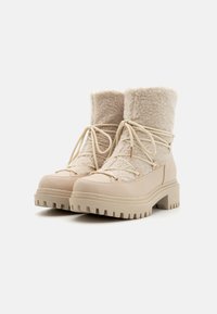 Jasnobeżowe botki do kostki, z gładką skórzaną dolną częścią i teksturowaną górną wykonaną z miękkiego materiału, z płaskimi sznurowadłami i wytrzymałymi podeszwami.