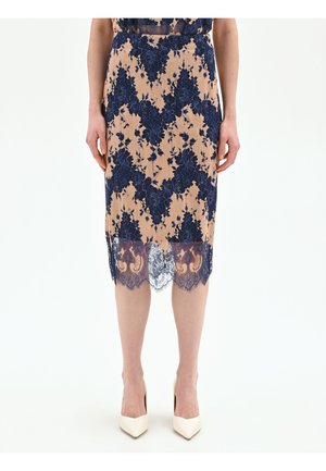 Gonna a matita beige con sovrapposizione di pizzo floreale blu navy, orlo in pizzo trasparente, indossata con décolleté bianchi a punta su sfondo neutro.