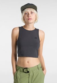 Kort mörkgrå linne med rund halsringning och en liten logga. Modellen matchar den med ljusgröna byxor som har en cirkulär spänne.
