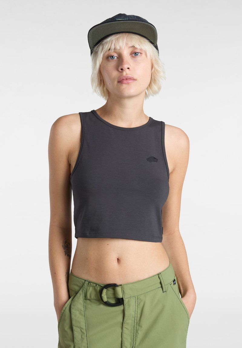 Kort mörkgrå linne med rund halsringning och en liten logga. Modellen matchar den med ljusgröna byxor som har en cirkulär spänne.
