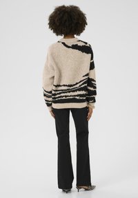 Pull beige avec motif abstrait noir, coupe décontractée. Associé à un pantalon noir évasé et des chaussures à imprimé zèbre.