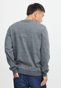 Grå strikkegenser med lange ermer, rund hals og ribbestrikket kant. Brukt over blå jeans, med en subtil teksturert finish.