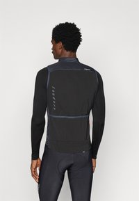 Must aktsentidega must rattavest, millel on keha külge puutuv disain, kerge kangas, reflekteerivad detailid ja lukuga tasku seljaosas.