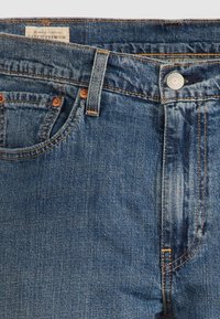 Džíny z tmavě modrého denimu s mírně vybledlým vzhledem, vybavené měděnými nýty, kovovým knoflíkem a štítkem na pase.