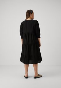 Black tiered dress with three-quarter puff sleeves, textured fabric, and a loose fit, designed for comfort and elegance.