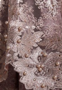 Spets i mjuk mauve med blommönster, dekorerad med texturerade pärlor och metalliska accenter i guld- och rosatoner.