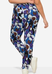 Patroonbroek met een meerkleurig ontwerp van abstracte gezichten in blauw, bruin en wit; elastische tailleband en taps toelopende benen.