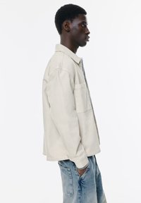 Beige denimjakke med afslappet pasform, forlommer og klassisk krave, parret med lyseblå slidte jeans.