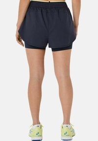 Shorts de sport bleu marine avec une taille élastique, design superposé et shorts de compression intégrés, associés à des chaussures de course de couleur claire.