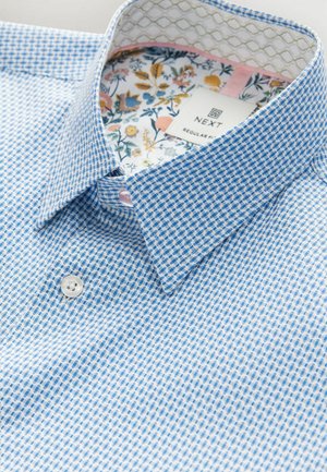 Camicia a quadri blu e bianca con colletto button-down, foderata con un motivo floreale all'interno del colletto e nei polsini. Chiusura con un bottone bianco.