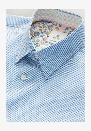 Niebieska i biała koszula w kratę z kołnierzykiem zapinanym na guziki, z kwiatowym wzorem wykończonym wewnątrz kołnierza i mankietów. Zapięta na biały guzik.