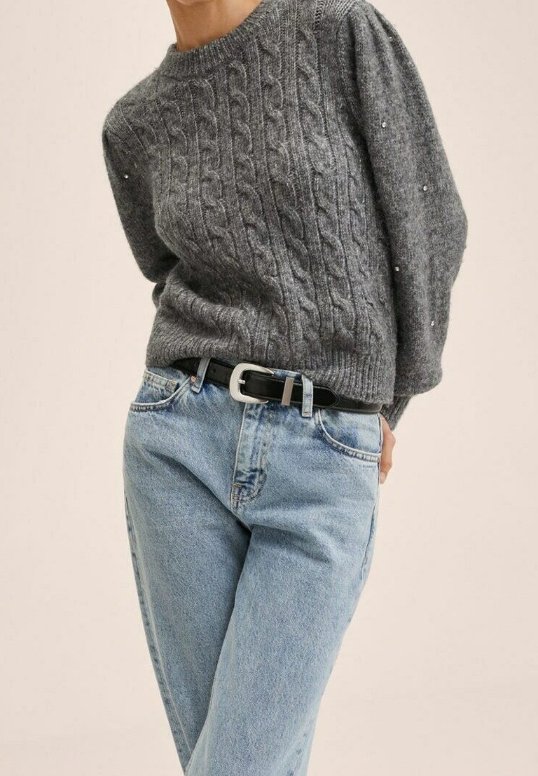 Personne portant un pull gris en maille torsadée avec de petites perles et un jean taille haute bleu clair avec une ceinture noire à boucle argentée.