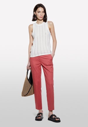 Weißes ärmelloses Top mit vertikalen Streifen, rosa maßgeschneiderte Hose, schwarze Sandalen und eine geflochtene Tragetasche. Schlicht und modern.