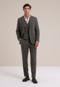 Siv tri delni suknjič z ožjim krojem, teksturirano tkanino in enorednim suknjičem. V kombinaciji z belo srajco in temnimi čevlji.