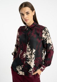 Czarna bluzka z maroonowymi i beżowymi kwiatowymi wzorami. Posiada kołnierzyk, zapięcie na guziki z przodu oraz długie rękawy. Lekko wygięty dół.