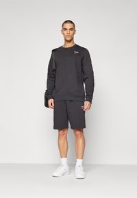 Ensemble en sweatshirt et shorts gris foncé, en mélange de coton. Comprend des poignets en côtes, des baskets blanches et un petit logo sur la poitrine et les shorts.