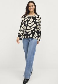 Zwart-witte bloemenblouse met lange mouwen, ronde hals en plooien, gecombineerd met lichtblauwe flared jeans en zwarte haklaarzen.