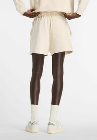 Beige cotton shorts with an elastic waistband and back pocket, paired with cream socks and light-colored sneakers.