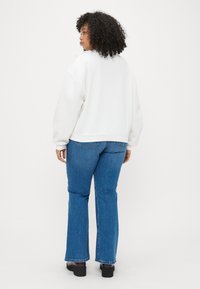 Hvid oversized sweatshirt med ribbede manchetter, parret med blå flagrende jeans. Glat tekstur, minimalistisk design og ensfarvet farveskema.