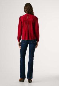 Blusa rossa con dettaglio a chiave sul retro, maniche lunghe a sbuffo. Abbinata a jeans a palazzo blu scuro e stivaletti marroni con tacco.