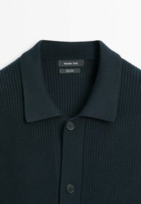 Donker marineblauwe gebreide cardigan met een geribbelde textuur, twee zwarte knopen en een kraag, met het label Massimo Dutti, 100% katoen.