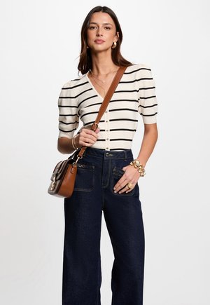 Striped, cream and black short-sleeve cardigan with buttons, paired with high-waisted, dark denim wide-leg jeans and a brown shoulder bag.