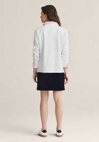 Vit långärmad topp med rosa färg på kragen, matchad med en marinblå kjol och vita sneakers. Snyggt tyg med avslappnad passform och uppvikta ärmar.