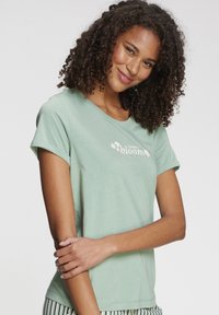 Svetlozelené bavlnené tričko s prehnutými rukávmi, na ktorom je nápis "vyber si kvitnúť" a kvetinové akcenty, v kombinácii s pruhovanými pyžamovými nohavicami.