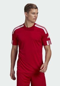 Maglietta sportiva rossa con strisce bianche sulle spalle, realizzata in materiale leggero, con colletto a girocollo e maniche corte. Logo Adidas sulla manica.