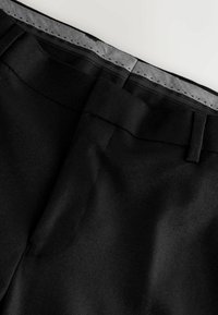 Black tailored trousers with a smooth texture, featuring a woven waistband, front pockets, and neat stitching details.