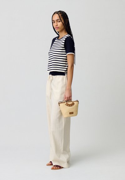 Haut à manches courtes rayé en bleu marine et blanc, pantalon large à rayures verticales crème, et un petit sac tissé avec une poignée marron.