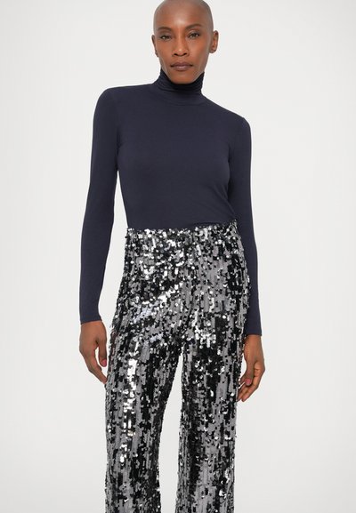 Un top turtleneck navy asortat cu pantaloni largi acoperiți cu paiete argintii. Material neted pe partea de sus; design strălucitor, texturat pe pantaloni.