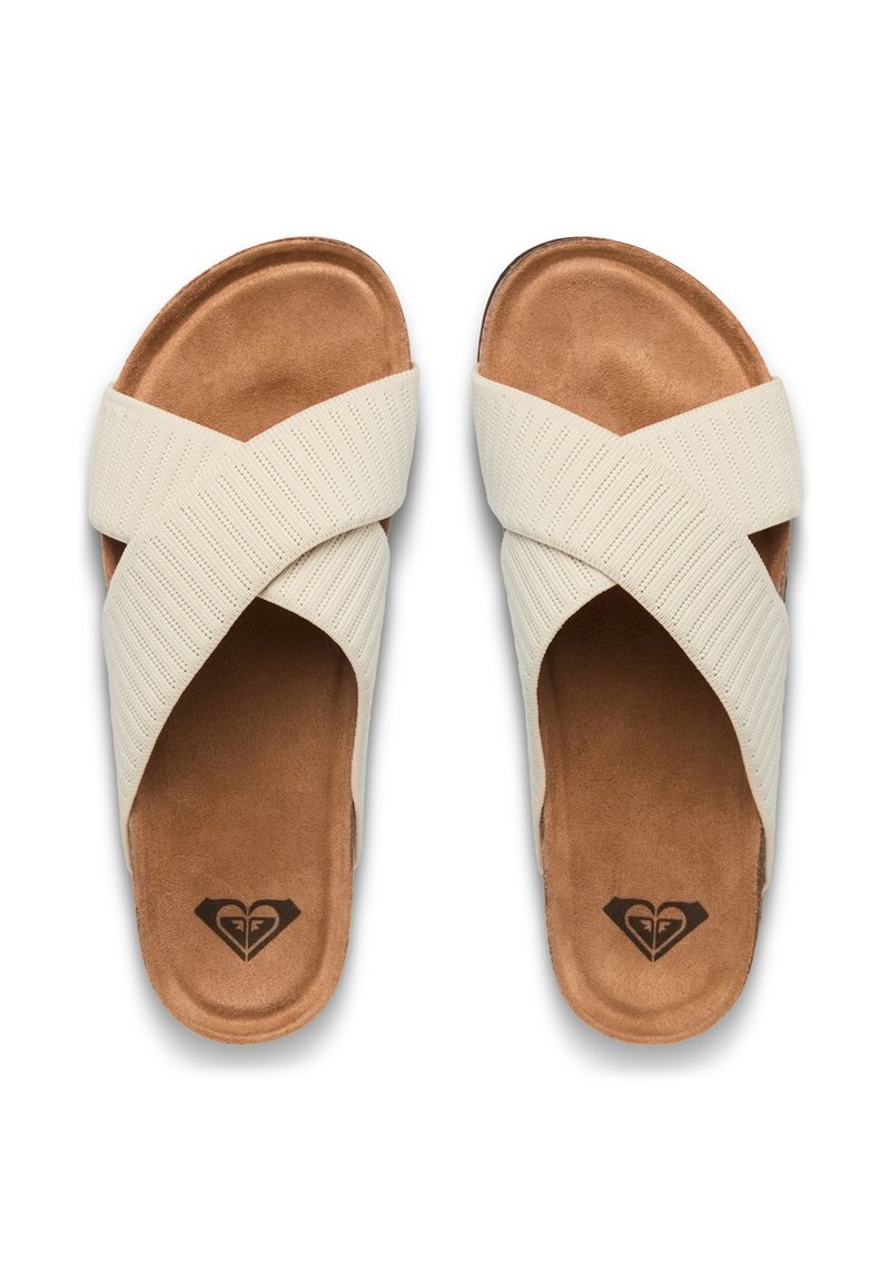 Sandali slide color crema con cinturini incrociati e testurizzati sopra una morbida soletta marrone, con un'impronta del logo a forma di cuore sul tallone.