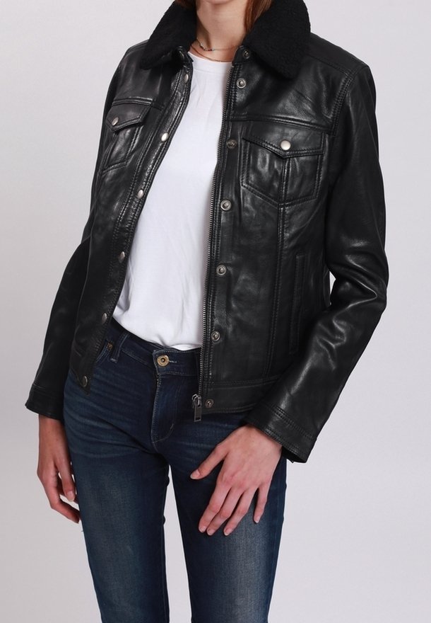 Femme portant une veste en cuir noire avec des poches poitrine à boutons et un col en peau lainée noire, sur un t-shirt blanc et un jean bleu.