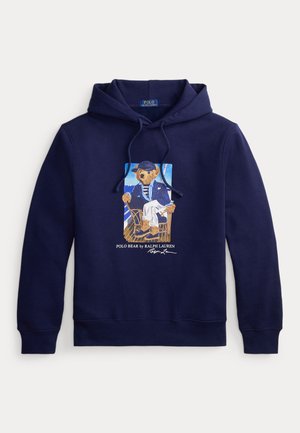 Marineblauwe hoodie met trekkoord, met een afbeelding van een beer in een matrozenoutfit zittend op een stoel met daaronder de tekst "Polo Bear by Ralph Lauren".