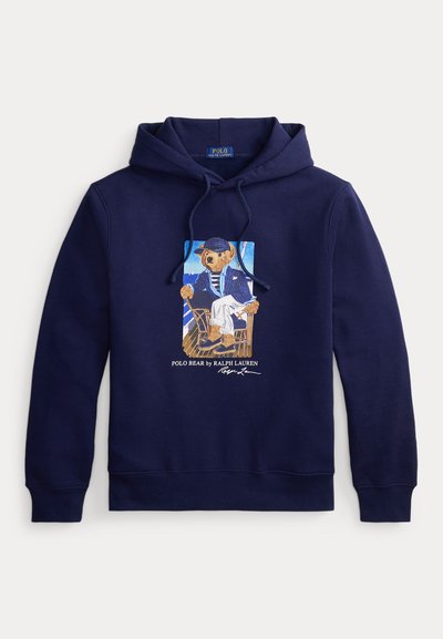 Μπλε σκουρόχρωμο hoodie με κορδόνι, με γραφικό ενός αρκούδου ντυμένου ναύτη που κάθεται σε καρέκλα και κείμενο "Polo Bear by Ralph Lauren" από κάτω.