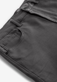 Close-up van donkergrijze broek met voorzak, riemlus, knoop en stoftextuur.