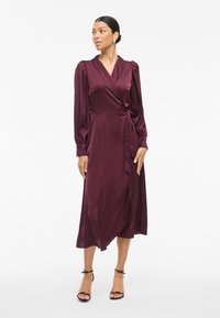 Burgundy satin wrap dress with long sleeves, a v-neckline, and a tie waist. Flowing midi-length skirt with soft, smooth texture.