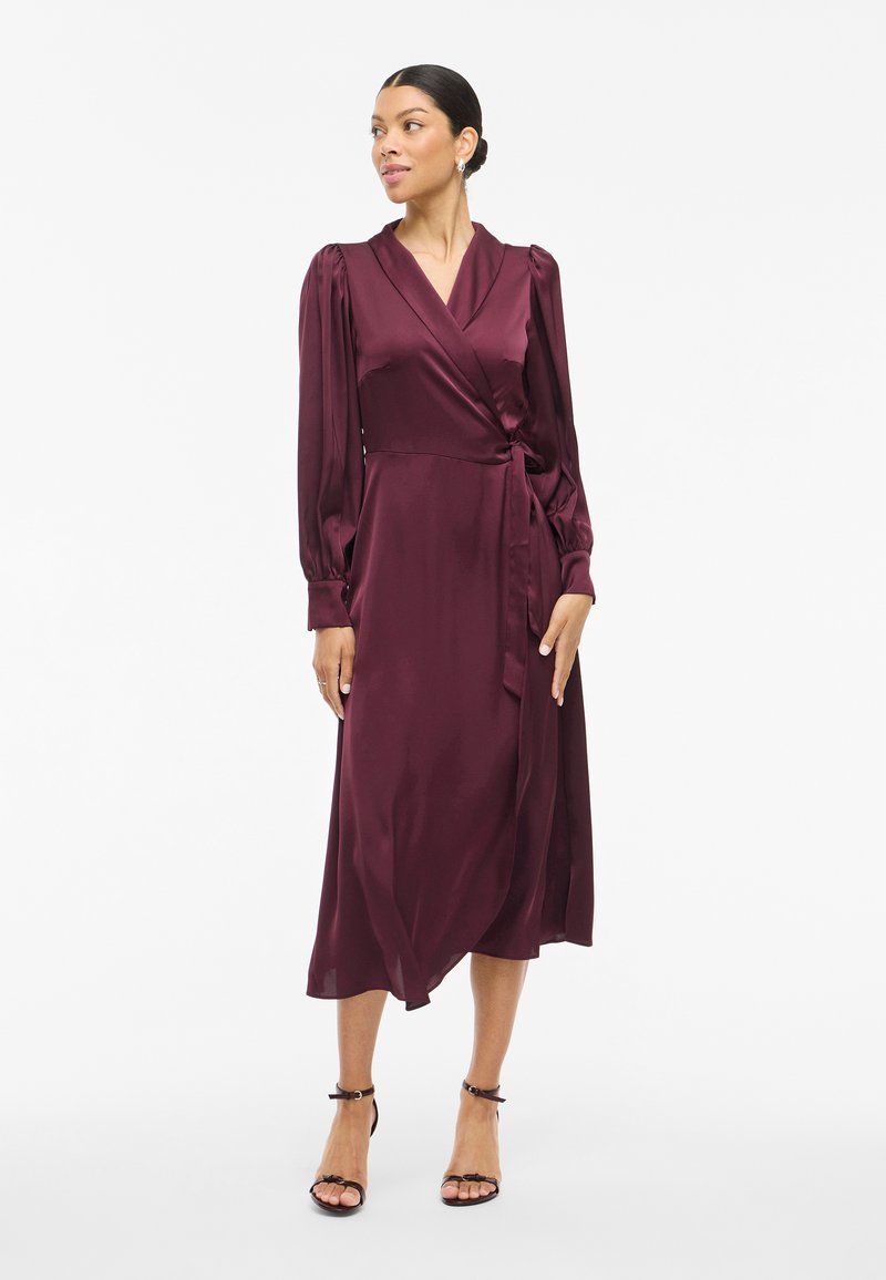 Burgundy satin wrap dress with long sleeves, a v-neckline, and a tie waist. Flowing midi-length skirt with soft, smooth texture.
