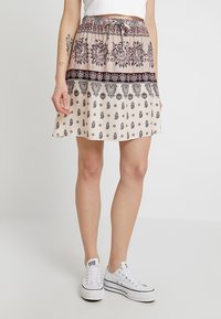 Lyhyt, laventuva hame beige-värissä, jossa on monimutkaisia mustia kuvioita ja nauhavyötärö. Yhdistetty valkoisiin lenkkareihin rentoa ilmettä varten.