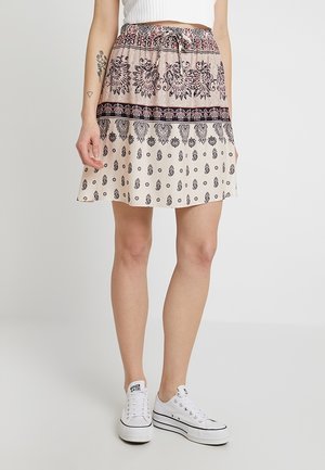 Gonna corta svasata beige, con intricati motivi neri e una vita con lacci. Abbinata a sneakers bianche per un look casual.