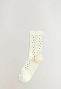 Cream-colored sock featuring a soft texture, dotted pattern in brown, ribbed cuff, and standard sock shape.