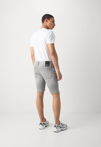 Gray denim shorts with a slim fit, visible stitching, and a back pocket featuring a black label. Paired with a plain white T-shirt and sneakers.