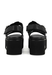 Sandali platform neri con suole spesse a righe, design aperto sul retro e larghe cinghie. Presentano dettagli con fibbie regolabili. Texture liscia.