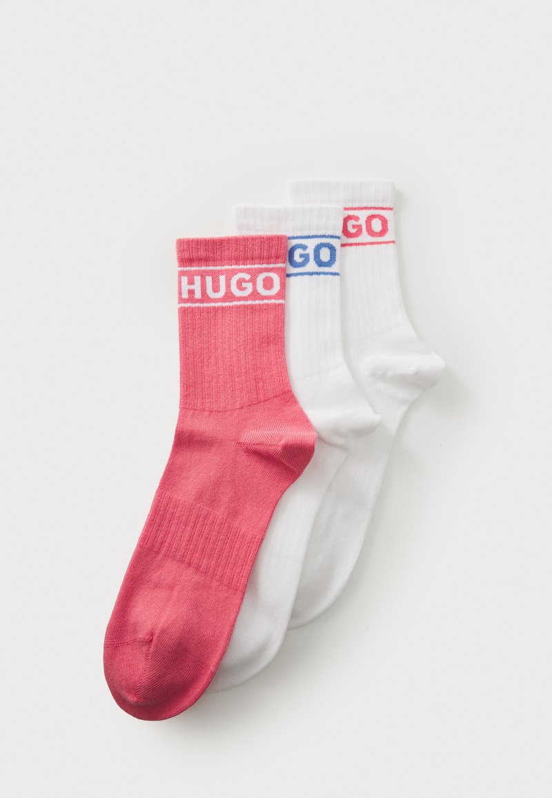 Sett med tre sokker: en rosa og to hvite. Hver har "Hugo" trykket på mansjetten. Glatt stoff med ribbet tekstur. Halvleggelengde.