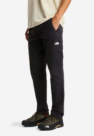 Czarne spodnie outdoorowe z kieszeniami na zamek i białym logo. Charakteryzują się luźnym krojem i trwałą tkaniną, odpowiednie do aktywnego użytkowania.