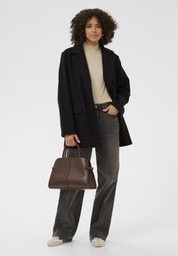 Čierny vlnený kabát cez béžový rolák, v kombinácii s tmavosivými širokými džínsami. Hnedá štruktúrovaná kabelka, smotanové tenisky s jemnými akcentmi.